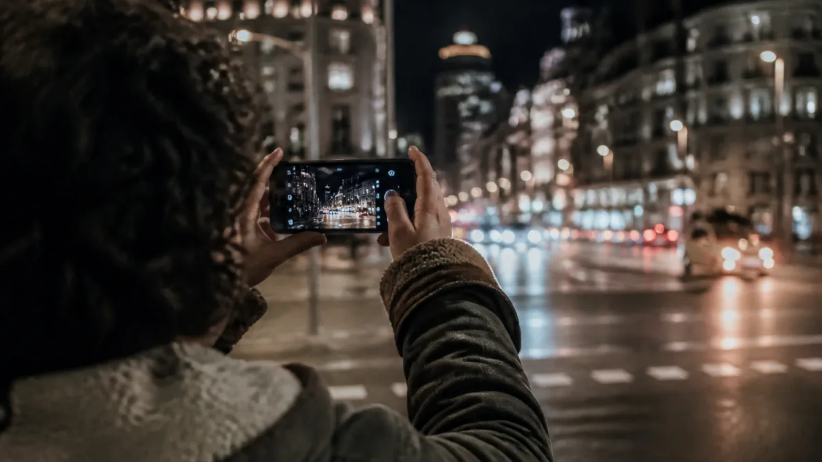 Pessoa fotografando uma rua iluminada à noite com celular