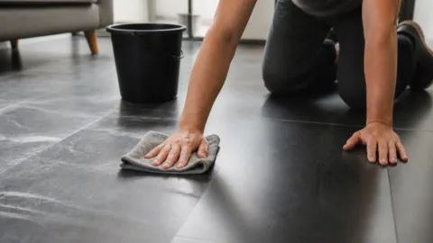 Pessoa limpando piso escuro com pano de microfibra
