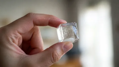 Mão segurando um cubo de gelo entre os dedos