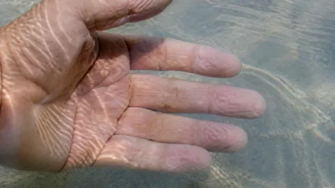 Dedos enrugados de uma mão dentro da água